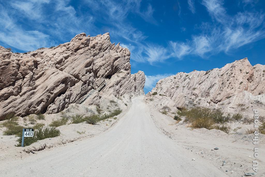 Bild Scheinbar führt die Schotterstrasse direkt in den Himmel. Valle Calchaquies, zeigt die Strasse in Mitten wilder Felsformationen mit schräg aufwärts gerichteten Schichtlinien darin.