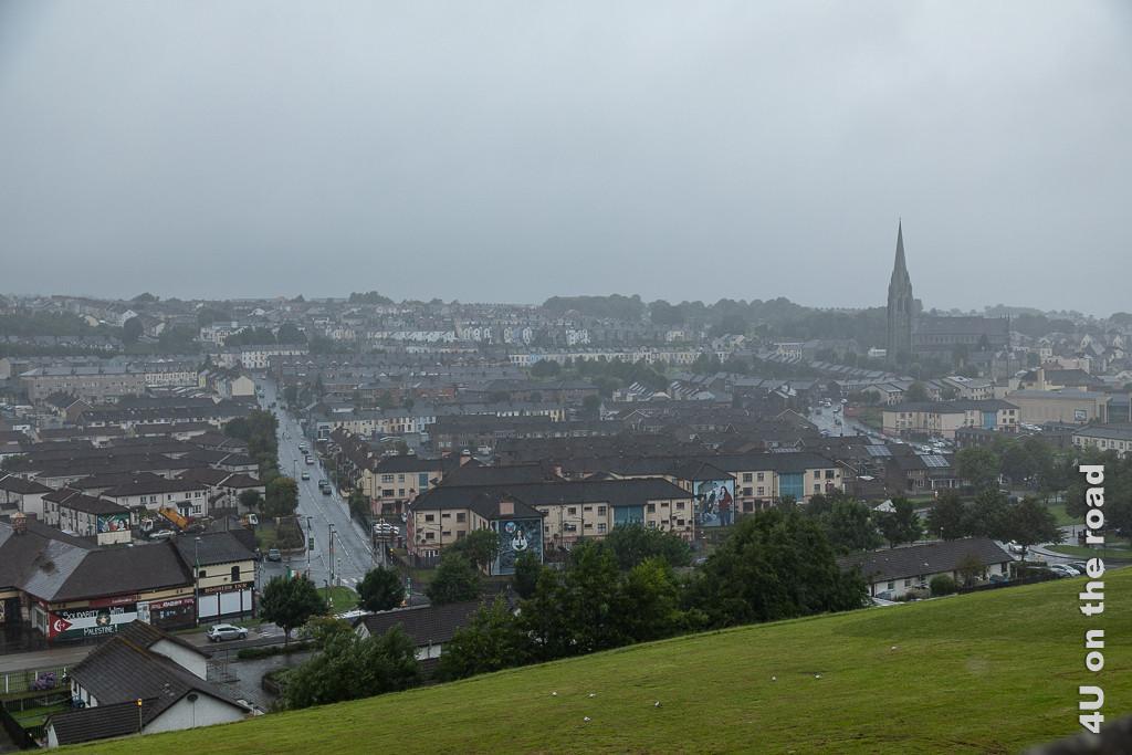 Bild Blick von der Stadtmauer Derry-Londonderry auf Häuser mit bemalten Fronten zeigt ein Häusermeer in Reih und Glied. Links teilt eine Strasse das Häusermeer, links erhebt sich eine Kirche.