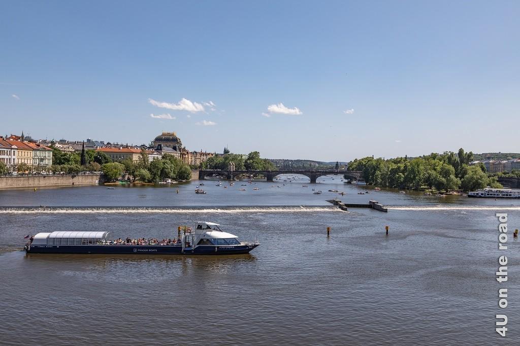 Bild Blick von der Karlsbrücke in Richtung - most Legií - Prag zeigt im Vordergrund ein an der Staustufe wendendes Ausflugsschiff, Strelecký Island, viele kleine Boote vor und hinter der Brücke, sowie die Häuser, die den Uferrand säumen.