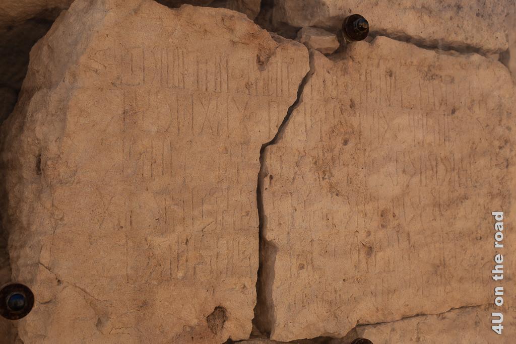 Bild Steintafel, die Auskunft über die Stadtgründung und den Namen der Stadt - Sumhuram gibt zeigt die in der Mitte gerissene Steintafel mit Schriftzeichen, die aussehen wie eine Mischung aus Hieroglyphen und Griechisch.