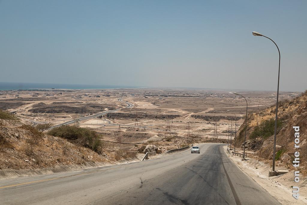 Auf dem Weg nach Salalah - Blick von oben auf die trockene Küste zeigt die sich zum Meer windende Strasse mit Laternen und Strommasten. Kein Grün erfreut das Auge