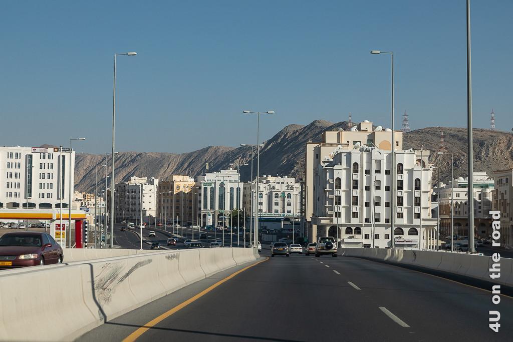 Muscat - Wohn- und Geschäftshäuser in arabischer Architektur beidseits der Autobahn. Rechts schmiegen sich die Häuser an die Berge.