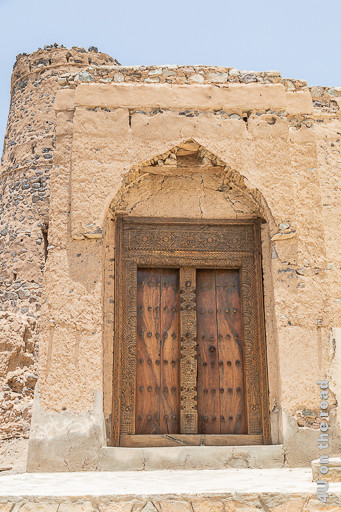 Al Mudayrib - dekorative Holztür. Diese Holztür schmückt ein nicht ganz intaktes Eingangsportal. Die Holzmaserung ist ist speziell. Die Balken an den Seiten, oben und in der Mitte sind kunstvoll geschnitzt. Metalldornen sind in 6 Reihen übereinander auf der Tür angebracht.