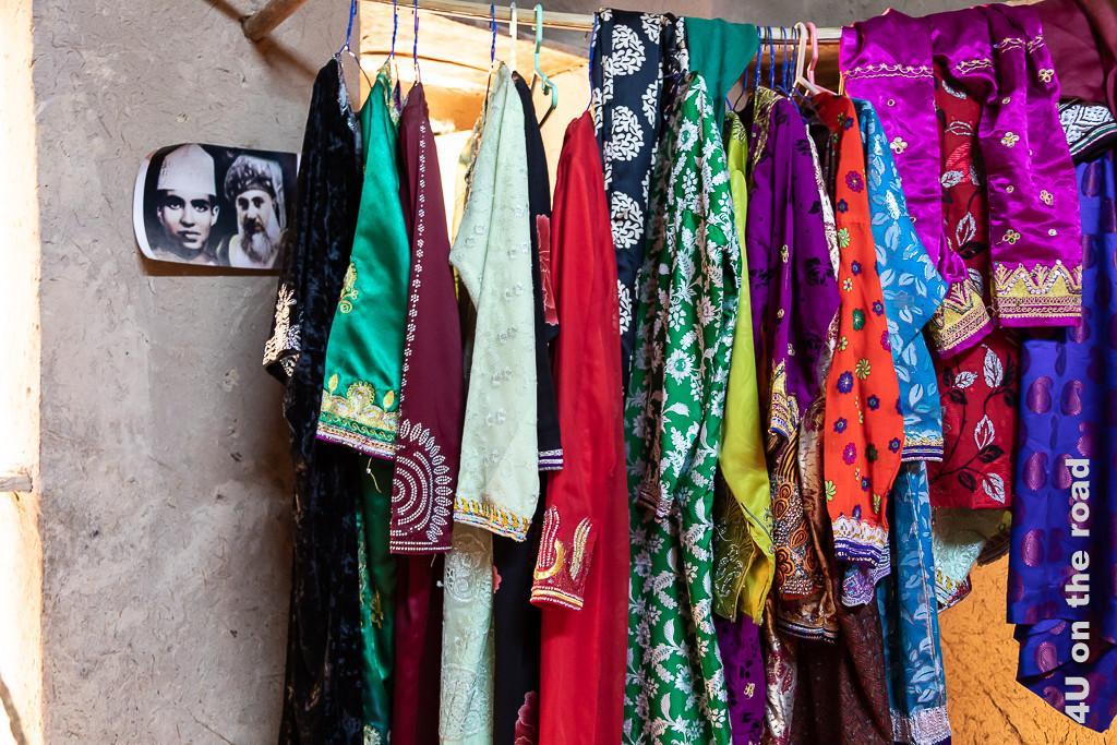 Im Museum Bait al Safah, Al Hamra - Die Kleider sind zum Teil aufwändig bestickt. Auf einer Kleiderstange hängen 14 Kleider und Hosen in den unterschiedlichsten Farben und Schnitten. Ein Foto vom Sultan als Kind und als alter Mann schückt den Raum.