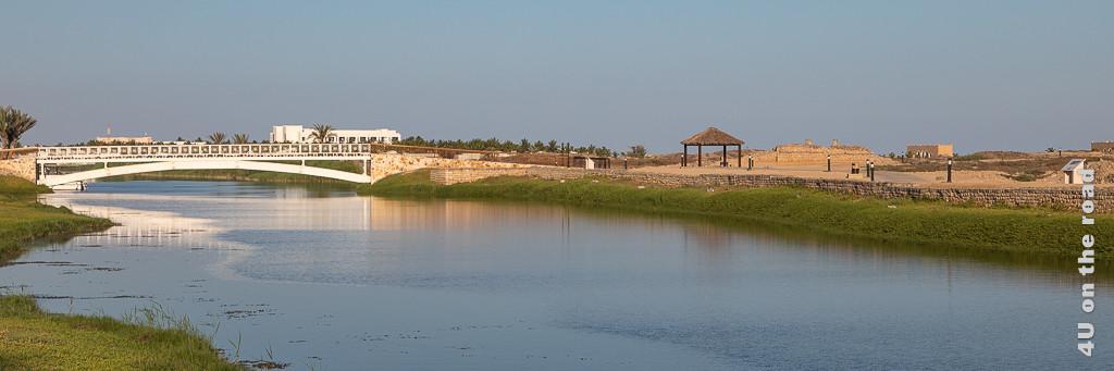 Al Baleed - Brücke über die Lagune zur Ausgrabungsstätte. Im Bild zu sehen sind Teile der Ausgrabung, die weisse Brücke und die Lagune