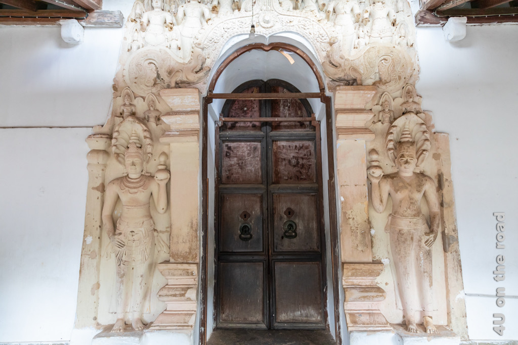 Eingang zur dritten Höhle des Dambulla Höhlentempels zeigt ein grosse Holztür. Neben der Tür befinden sich Säulen und Steinfiguren, die die Tür umrahmen.