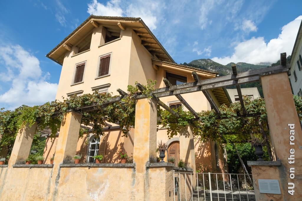 Die Villa Garbald in Castasegna mit ihrem pastellfarbenen Anstrich, der grossen von Wein beschatteten Terrasse, im unteren Teil Terrassenfenstern mit Rundbögen, ragt 3 Etage in die Höhe. Unter dem Dach scheint es noch eine gedeckte Aussichtsterrasse zu geben. 