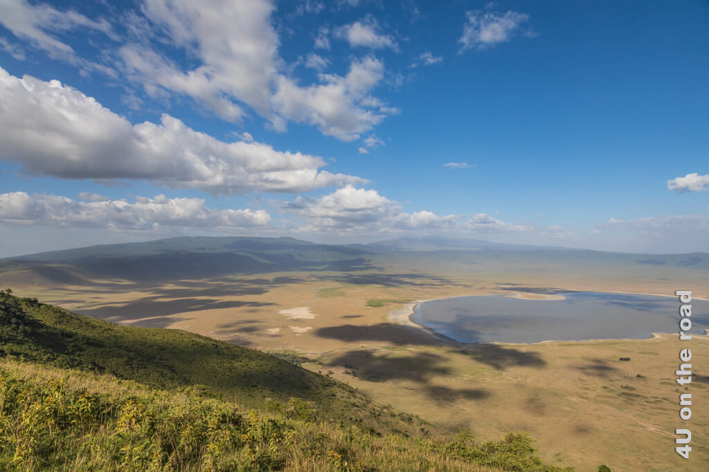 Die Aussicht in den Krater am Ende unserer Wanderung entlang des Ngorongoro Kraterrands ist beeindruckend. Ein grosser See ist in der Mitte zu sehen und schwarze Punkte, die Büffel sind.