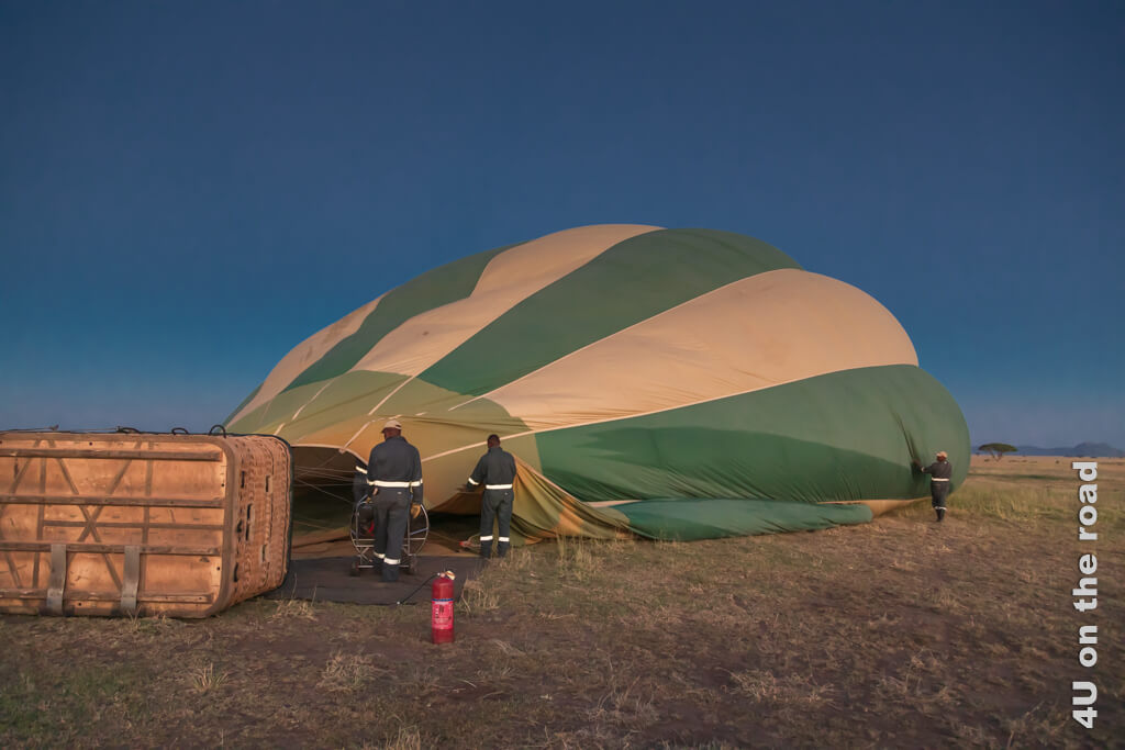 Die Ballonhülle mit grünen und beigen Abschnitten im Wechsel liegt erst leicht aufgeblasen auf der Seite, genauso wie der Transportkorb. Die Ballonfahrt über der Serengeti ist unsere erste Ballonfahrt, so dass wir alles gespannt beobachten.