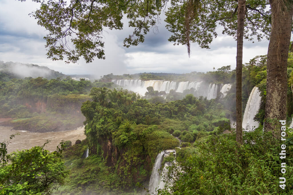 Ein Blick auf die Wasserfälle von Iguazú von der argentinischen Seite. Der dichte Urwald, die Gischt in der Luft und mehrere Wasserfälle bei stark bewölktem Himmel. Mit unseren Besichtigungstipps für die Wasserfälle von Iguazú wären wir hier nicht von einem tropischen Regenguss so auf dem falschen Fuss erwischt worden.