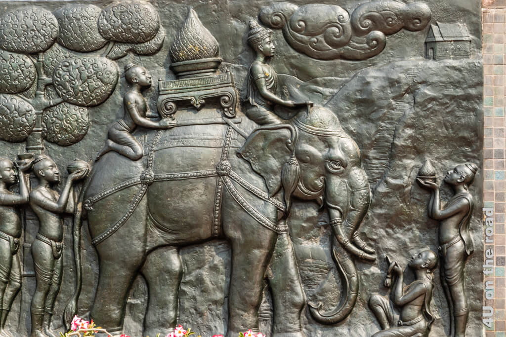 Bronzebild mit geschmücktem Elefant der vielleicht eine Stupa trägt. Eine Person reitet ihn hinter dem Kopf sitzend, die andere Person schaut dass die Stupa nicht herunterfällt. Vor und hinter dem Elefanten reichen Leute Gaben.