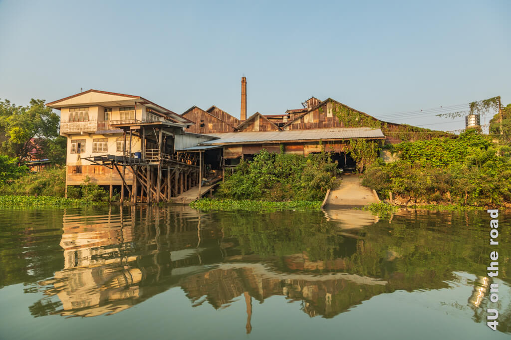 Eine alte, mystisch von Pflanzen berankte Fabrik mit Wohnhaus spiegelt sich im Fluss - Besichtigungstipps Ayutthaya