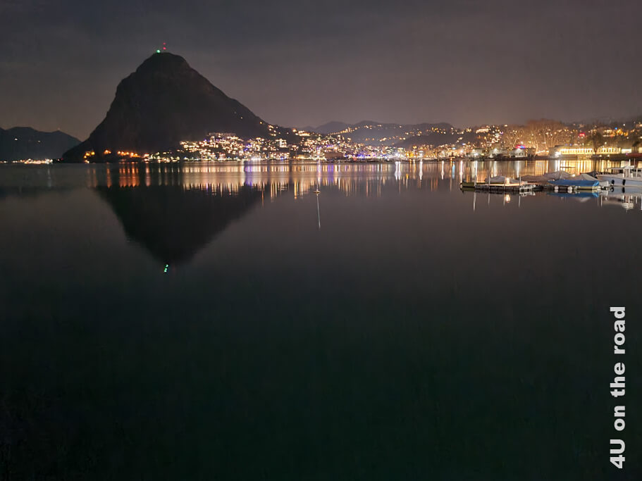 Der Monte San Salvatore spiegelt sich im See genauso wie die Lichter der Stadt. Frühling in Lugano