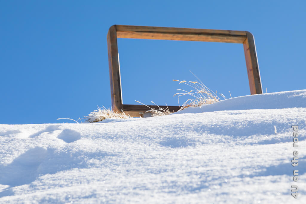 Ein grosser Holzrahmen steht als Posten 4 des Fototrails Sörenberg in der Landschaft und hebt sich aus dieser Perspektive vom Himmel ab. Er bildet einen würdigen Rahmen für vereiste Gräser.