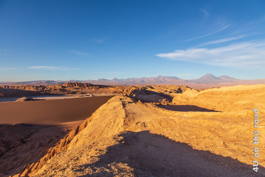 Das Valle de la Luna zum Sonnenuntergang in Braun- und Oranget&ouml;ne getaucht. Berge und Sand, w&auml;hrend sich im Hintergrund hohe Vulkane erheben. Reisetipps Chile von A - Z