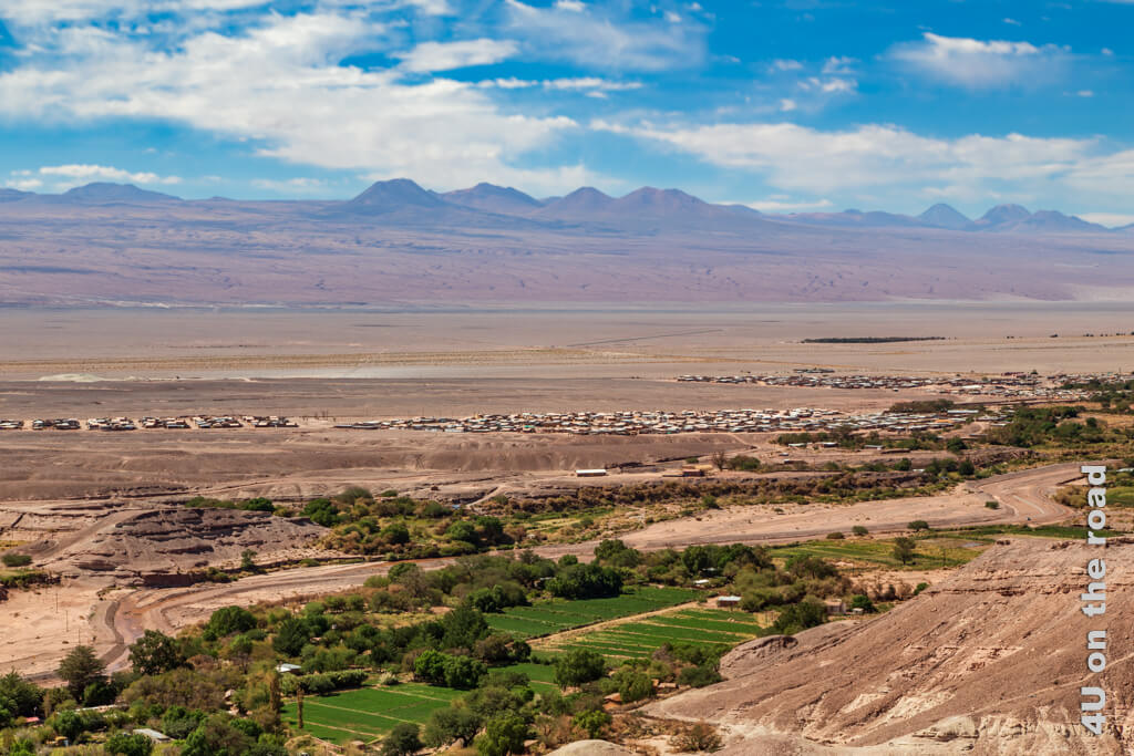 Oberhalb der Sehenswürdigkeit der Ruine Pukara de Quitor geht es zu einem Aussichtspunkt auf den Berg. Von oben sieht man die Facetten der Atacama Wüste: grüne Felder, Büsche und Bäume. Auf einer Ebene ziehen sich Häuser entlang. Im Hintergrund ragen Vulkane und Gipfel in den Himmel. Blauer Himmel, rötlicher bis gelblicher Boden und das fehl am Platz wirkende Grün geben einen Eindruck von der Wüste wieder. Sehenswürdigkeiten in der Atacama Wüste