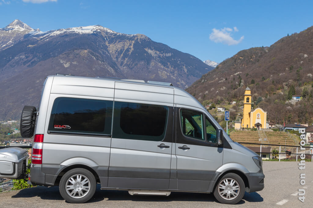 Unser Wohnmobil mit Transportkiste und Reserverad an der Hecktür vor der Bergkulisse der Berge in Belinzona. Wohnmobil Reisen und Tipps