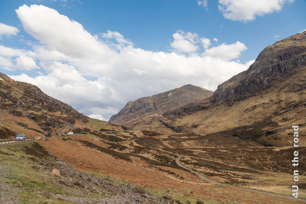 Die Strasse folgt dem Verlauf des Glen Coe Tals durch das schottische Hochland und steigt sanft an. Die Hügel scheinen sich zur Strasse zu neigen. Unterhalb der Strasse führt ein Wanderweg durch.