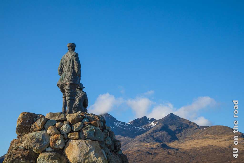 Zwei Männer in Tweethosen und Mütze blicken den Gipfeln der Cuillin entgegen. Ein schönes Denkmal.