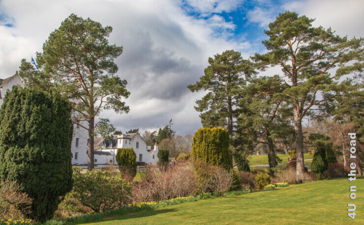 Durch grosse Kiefern und in Form geschnitte Bäume erhascht man einen Blick auf Blair Castle. Für einen Moment reisst der Himmel auf und zeigt ein kleines Stück Blau. Feature für den Beitrag von Edinburgh zur Isle of Skye,