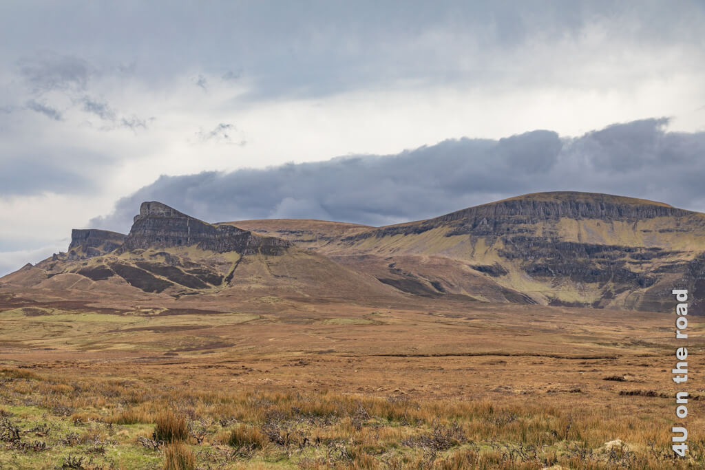 Steile Klippen ragen schräg aus den sonst abgerundeten Hügeln. Noch ist das Gras weitestgehend braun. Dunkle Wolken dramatisieren die Szenerie. Die Quiraing sind eines der Highlights auf der Isle of Skye.