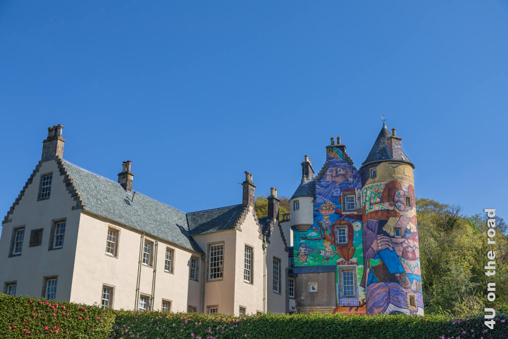Blick von vorn auf Kelburn Castle. Der neuere Anbau ist im Stil eines französischen Landhauses, während der alte Flügel des ursprünglichen Hauses mit Turm in farbenfrohen Graffiti leuchtet. 