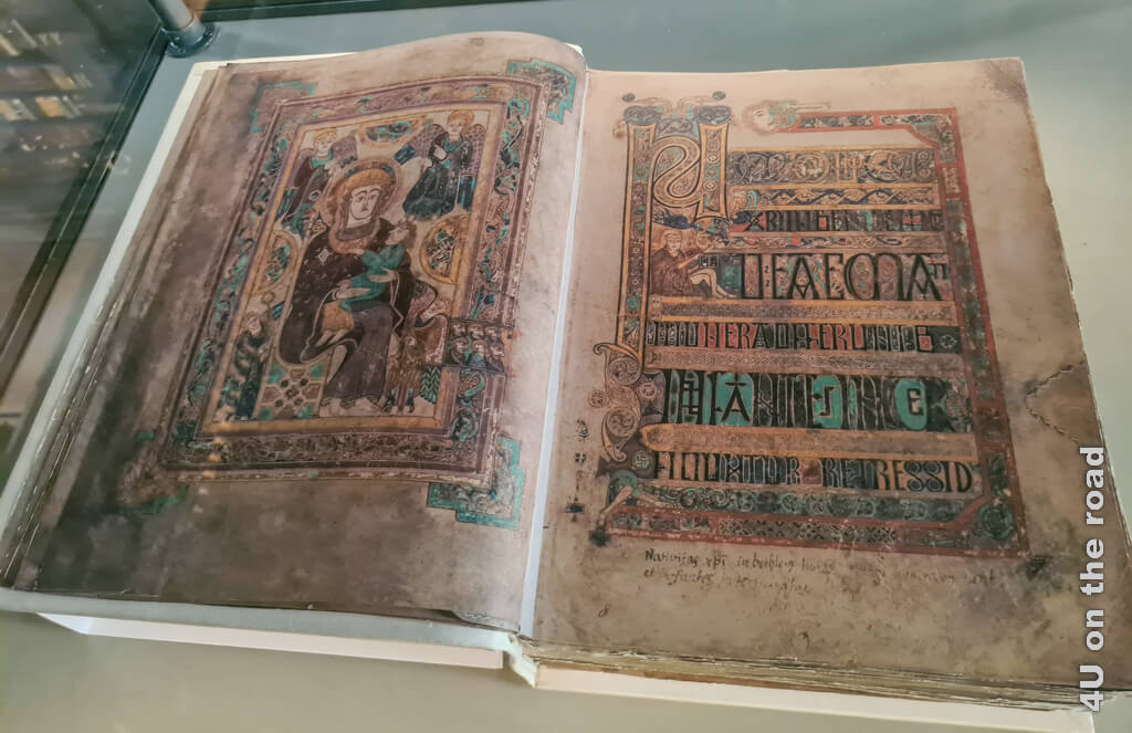 Faksimile des Book of Kells. Die linke aufgeschlagene Seite zeigt ein kunstvoll verziertes Bild. Auf der rechten Seite befindet sich Text mit unglaublich filigranen Verzierungen und Bildern. Trinity College Library - Dublins berühmteste Sehenswürdigkeit
