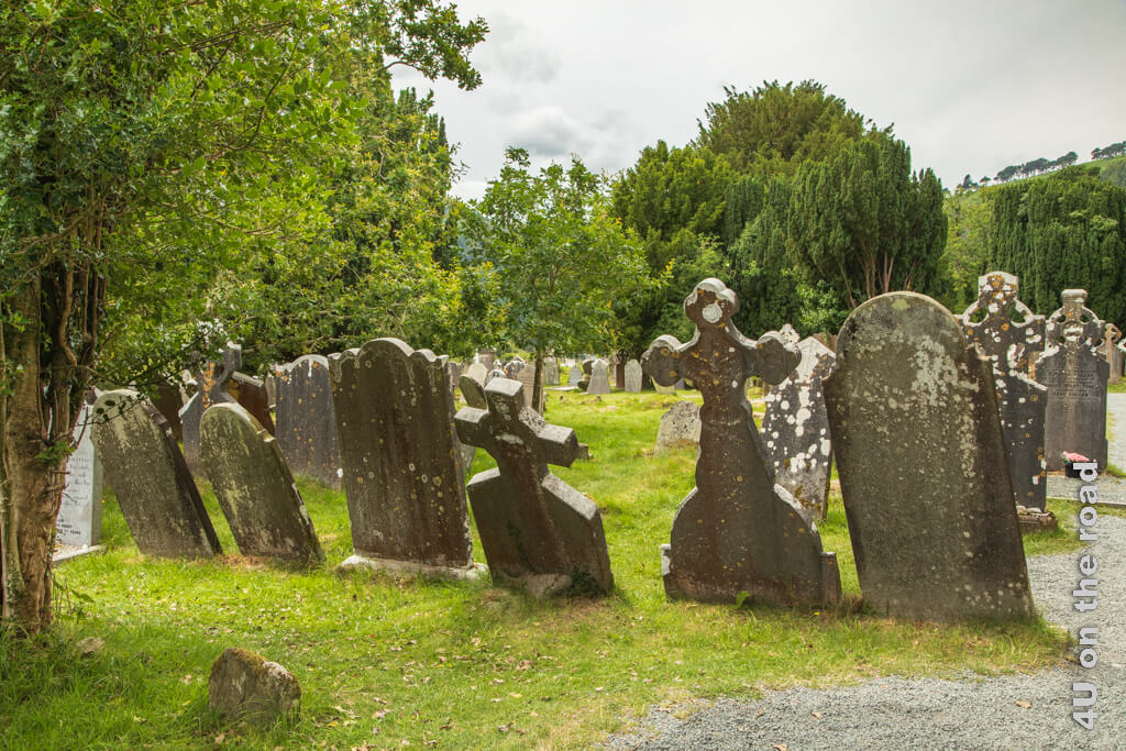 Grabsteine stehen auf dem Friedhof von Glendalough schief im Gras und sind von Flechten überzogen. Glendalough ist ein beliebtes Ausflugsziel in den Wicklow Mountains.