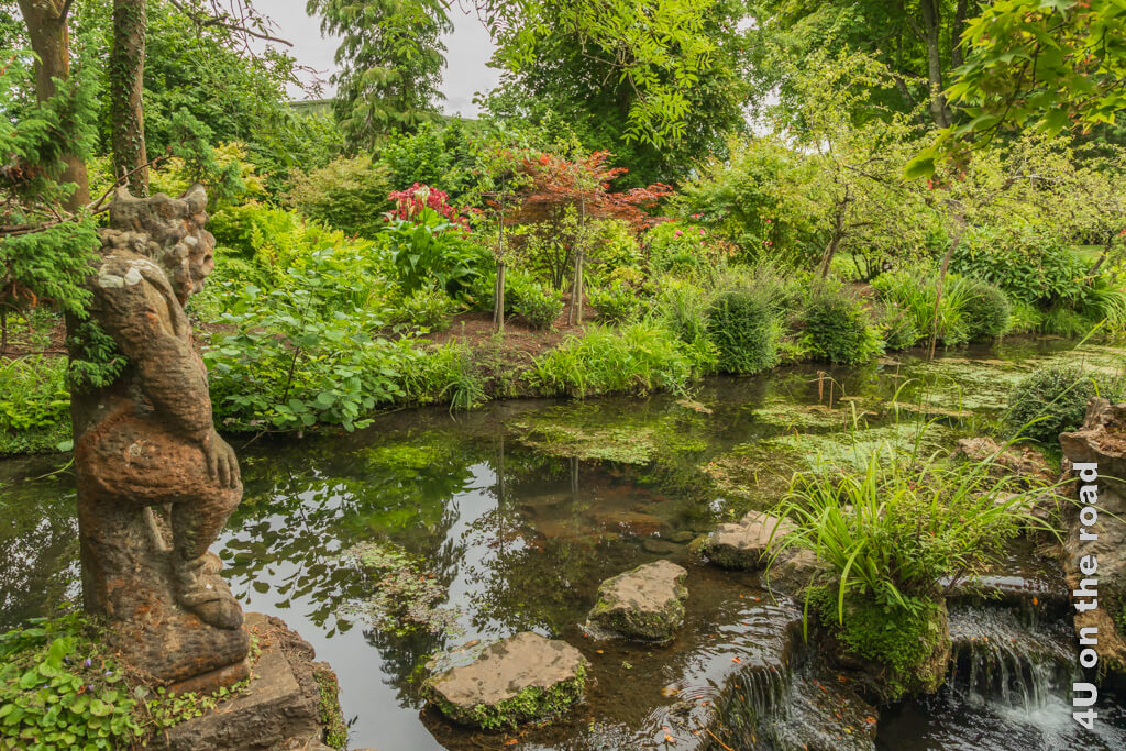 Ein Teil des Flusswassers biegt in einer kleinen Kaskade ab. Die Trittsteine zur anderen Uferseite werden von einer sitzenden Skulptur bewacht. Wofür diese Skulptur im japanischen Garten des irischen Nationalgestüts wohl steht?