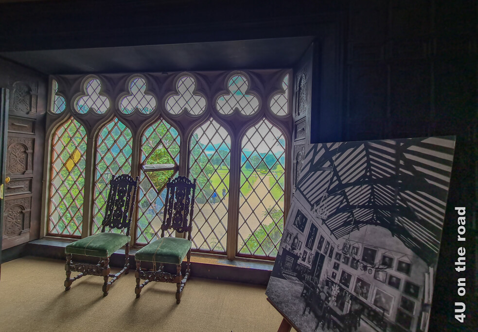 Blick vom Oak Room auf die weitläufigen Grünanlagen. Zwei kunstvoll geschnitzte Stühle vom Esstisch stehen vor der Fensterfläche, die aus 5 nach oben geschwungenen einzelnen Fenstern besteht. Zwischen den Bögen befinden sich weitere Fenster, zusammengesetzt aus je drei Kreisen.