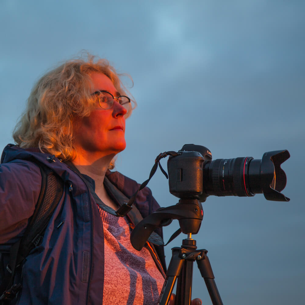 Susan schaut über die auf dem Stativ stehende Kamera in den Sonnenuntergang