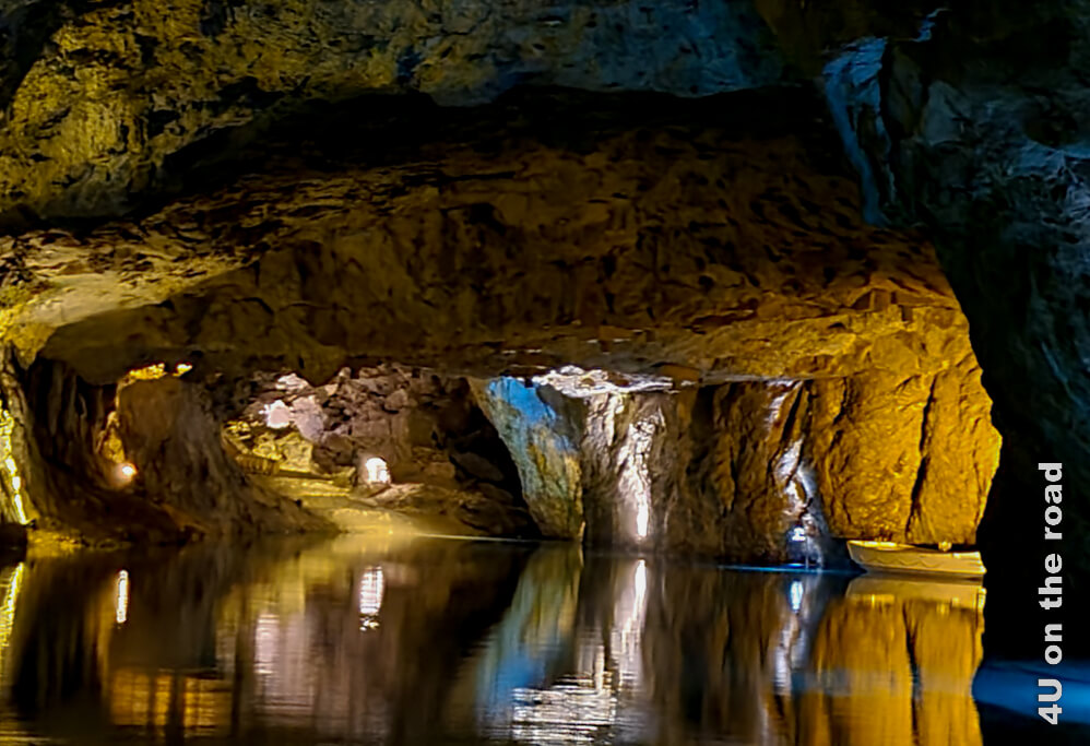 Lichter funkeln im Dunkel der Höhle und im Wasser des unterirdischen Sees St. Léonard im Wallis. Die Felsen spiegeln sich im Wasser.