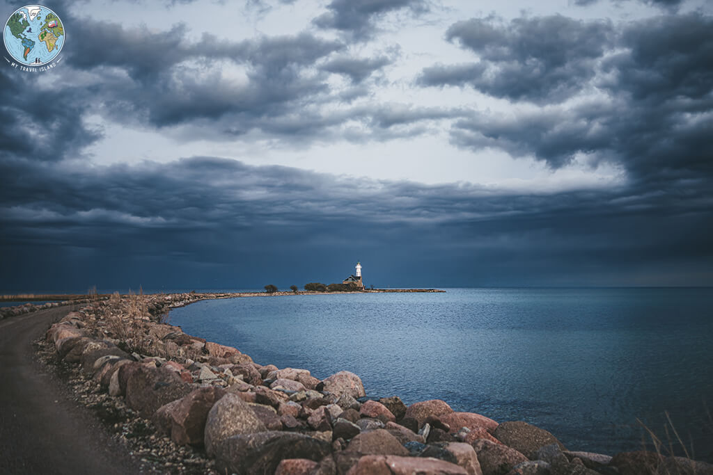 Fin Strand Öland zeigt einen weissen Leuchtturm am Ende der Bucht in einer Gewitterstimmung