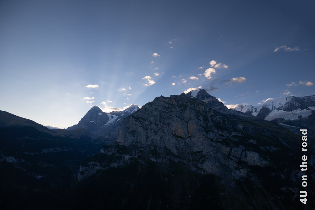 Die Bergwelt rund um Eiger, Mönch und Jungfrau wird von hinten erleuchtet. Gebündelte Strahlen erhellen den Himmel. Sonnenaufgang von Mürren aus gesehen.