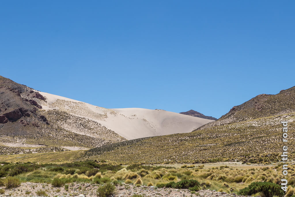 Feinster Sand bildet eine hohe Düne, die in einen Berghang mündet. 
