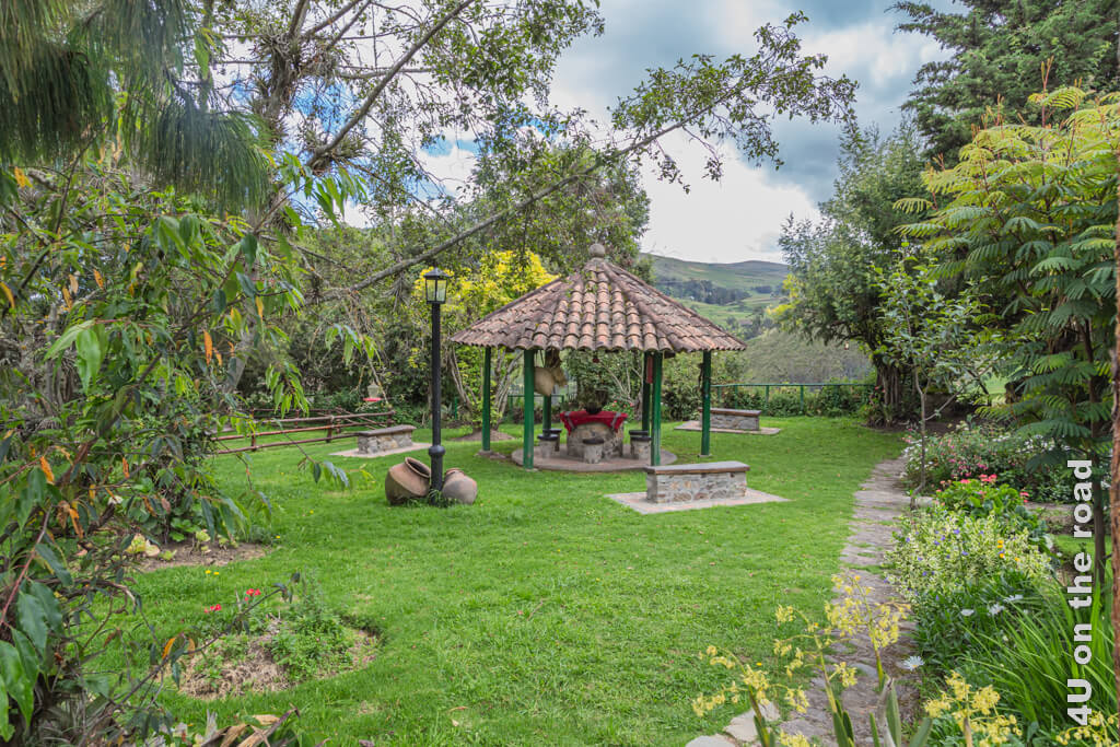 Einer von mehreren Gartensitzplätzen mit Blumenbeeten, Aussicht und einem kleinen überdachten offenen Pavillon und schattenspendenden Bäumen.