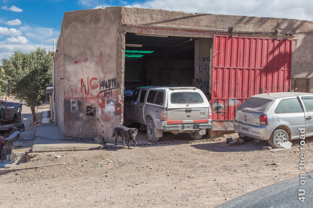 Ein viereckiges Gebäude mit Graffitis und einem grossen roten Schiebetor und einer grünlich schimmernden Innenbeleuchtung ist die Werkstatt in Humahuaca.