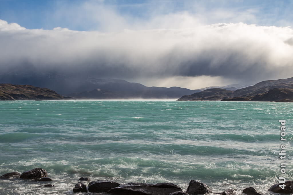 Der Lago Pehoe wirft grosse Wellen ans Ufer. Eine Regenwolke wie ein dicker Wurm rollt sich näher und wirkt bedrohlich.