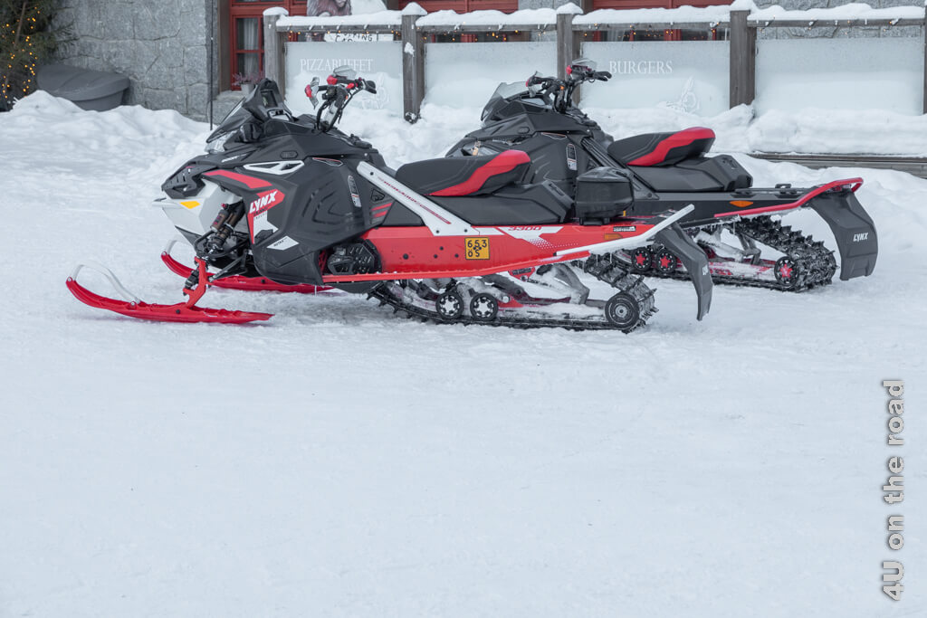 Zwei rote Motorschlitten halten vor einem Restaurant. Motorschlitten sind ein verbreitetes Fortbewegungsmittel in Rovaniemi im Winter.