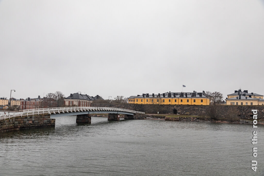 Eine Brücke mit weissem Geländer führt auf die Insel Pikku Mustasaari (eine von mehreren Inseln die zur Seefestung Suomenlinna gehört), die mit ihren leuchtend gelben Häusern heute ein wenig für Stimmung sorgt.