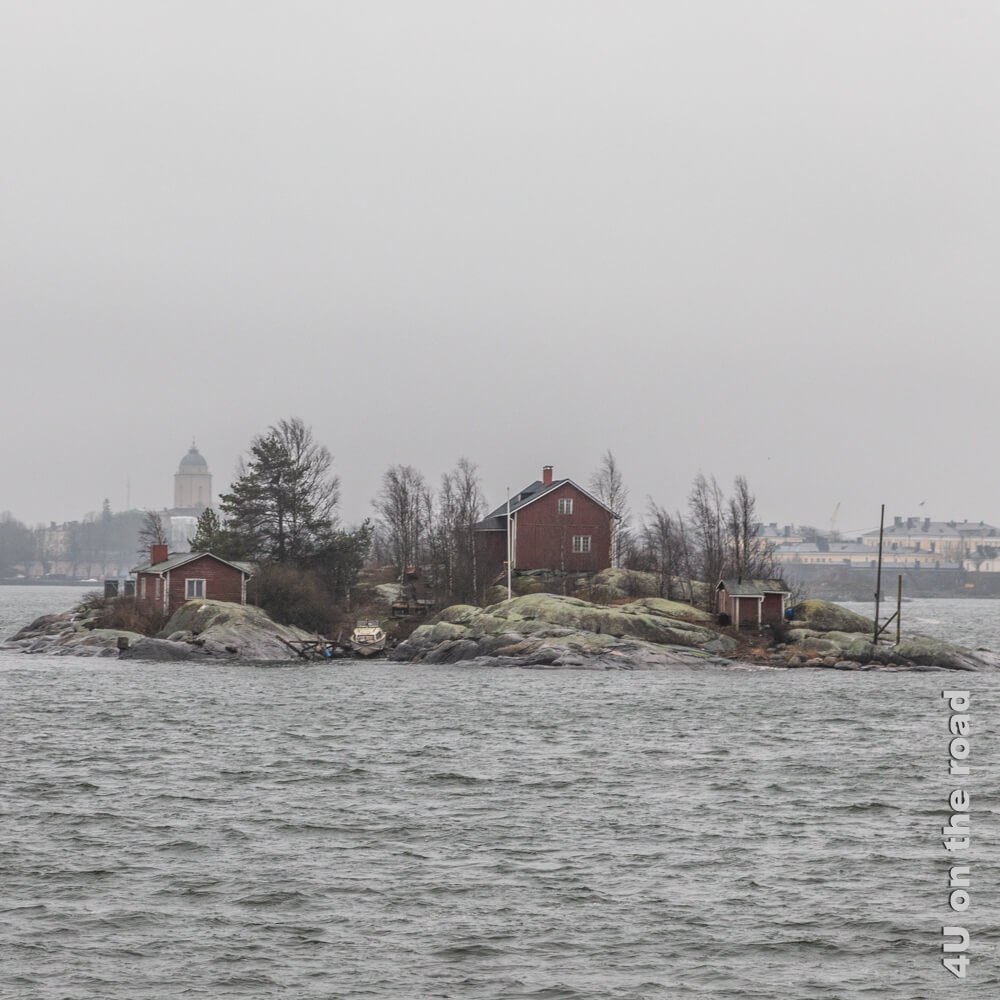 Eine Felsinsel mit einem roten Wohnhaus und einem kleinen roten Haus und Boot. Auf dem Weg zur Seefestung Suomenlinna