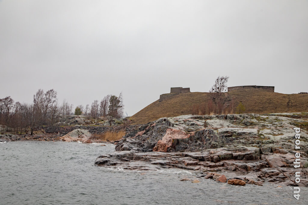 Blick über das Meer auf die grasbewachsenen Verteidigungsanlagen der Seefestung Suomenlinna.