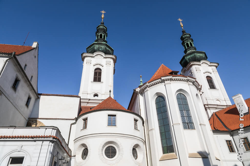 Kloster Strahov aus dem Innenhof fotografiert. Mit seinen Türmen und Seitenschiffen im Kontrast zwischen blauem Himmel, weisser Kirche mit roten Dächern und Kupfernen Türmen ist es wunderschön.
