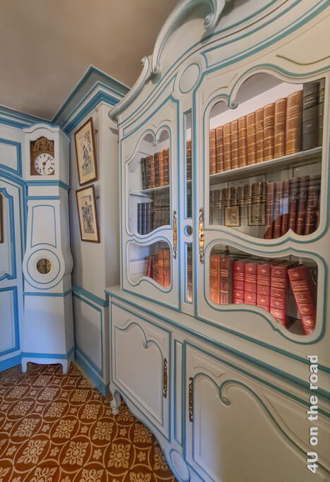 Der Bücherschrank mit Glastür ist hellblau mit geschwungenen mittelblauen Linien. In der Ecke steht eine farblich passende Standuhr in Monet's Haus in Giverny