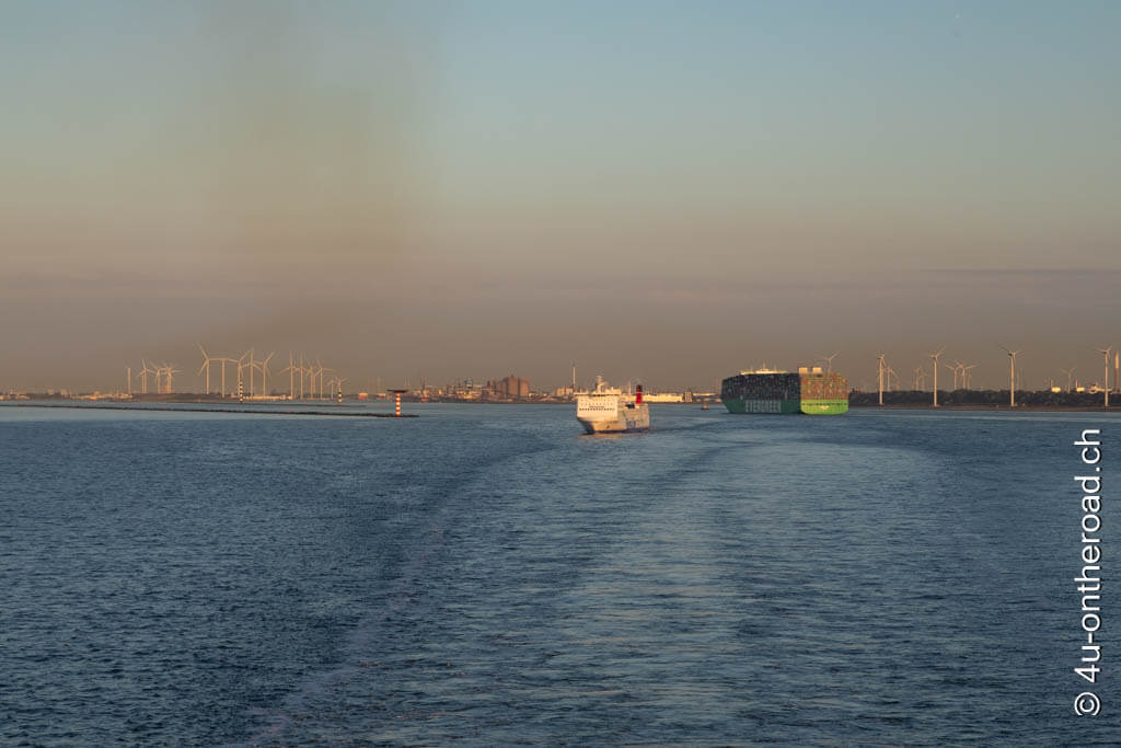 Windräder, eine Fähre, ein Containerschiff im Licht der untergehenden Sonne bei der Ausfahrt aus dem Hafen in Rotterdam. Anreise Roadtrip Schottland