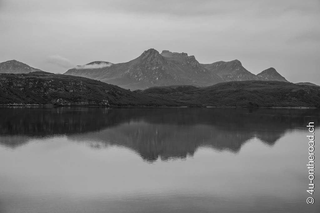 Berggipfel mit Spiegelung im See in schwarz-weiss. So düster kam uns der Tag auf unserem Roadtrip durch Schottland vor.