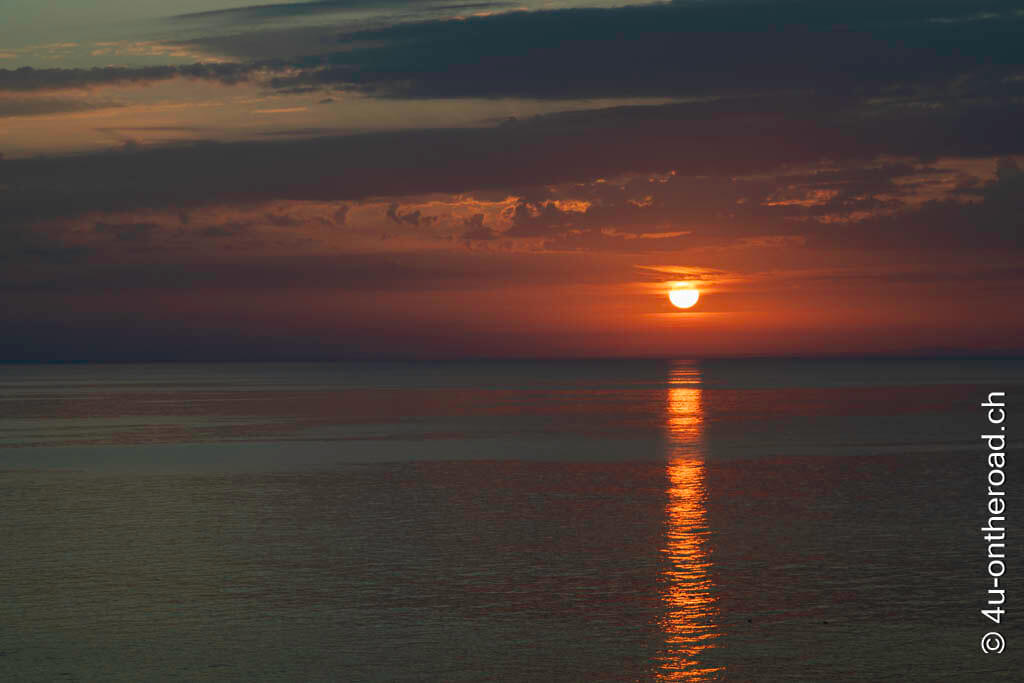Ein schöner Sonnenuntergang zum frühen Abend mit einer runden Sonne, die fast ins Meer fällt