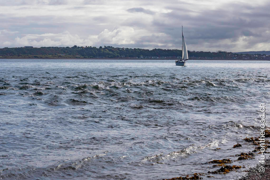 Ein Segelboot fährt mit Rückenwind am Chanonry Point vorbei etwas ausserhalb der sich treffenden Strömungen. Roadtrip durch Schottland mit dem Wohnmobil