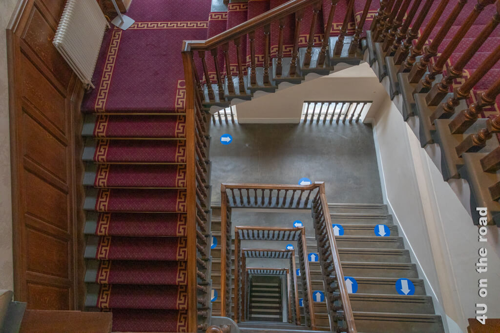 Das Treppenhaus in den City Chambers von Edinburgh mit Holzverkleidung, Teppichen und blau-weissen Pfeilen führt weit nach unten.