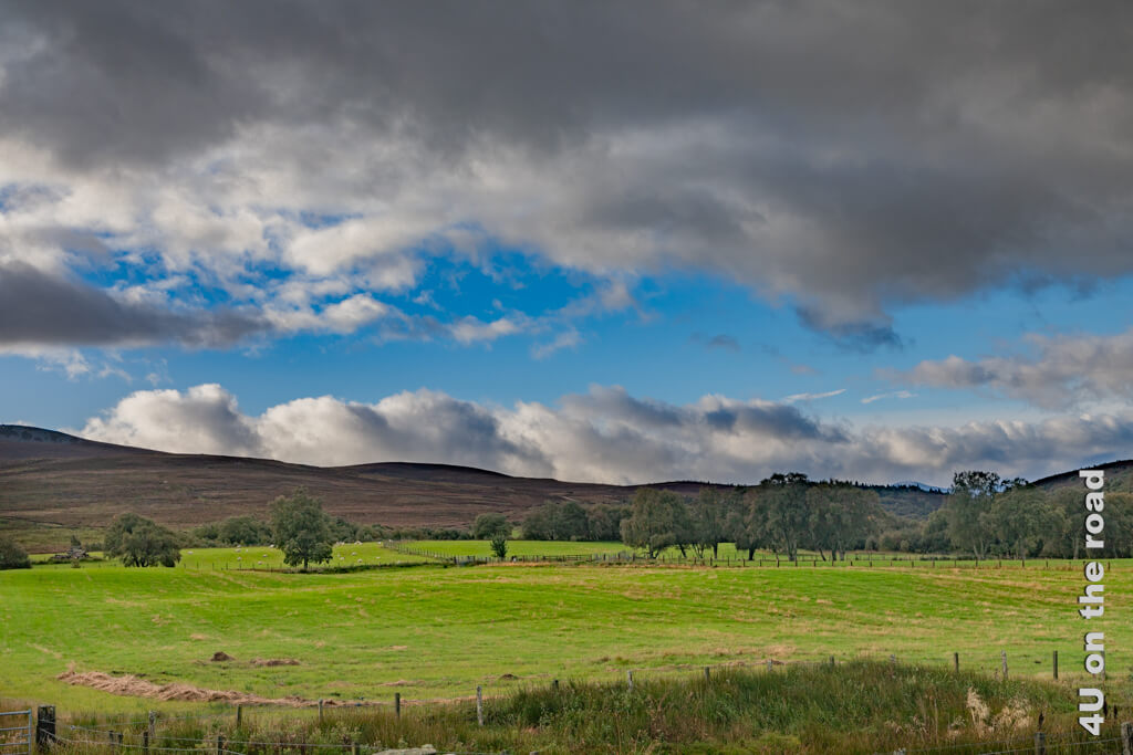 Blauer Himmel, dunkle Wolkenbänder, grüne Wiesen und die kahlen Hügel der Cairngorms - Morgenstimmung.